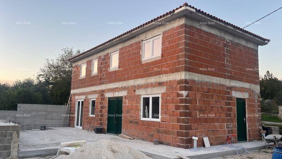 Rohbau eines Hauses mit roten Ziegelwänden, weißen Fenstern und grünen Türen bei Sonnenuntergang.