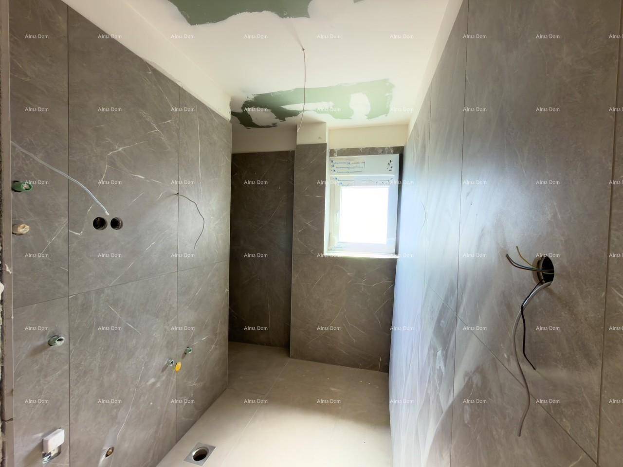 Unfertiges Badezimmer mit grauen Fliesenwänden, Fenster und vorbereiteten Anschlüssen.