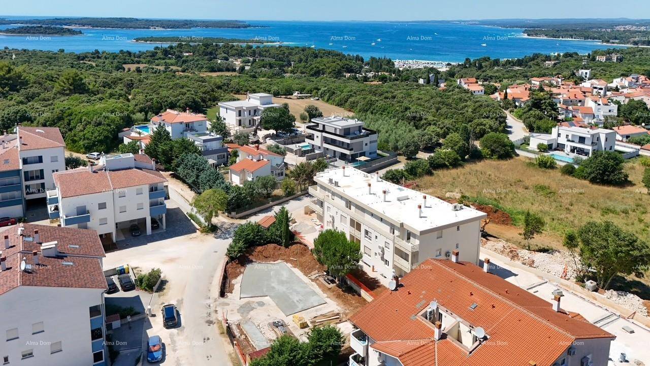 Weitläufige Luftaufnahme einer Küstenlandschaft mit Wohngebäuden, viel Grün und dem Meer im Hintergrund.
