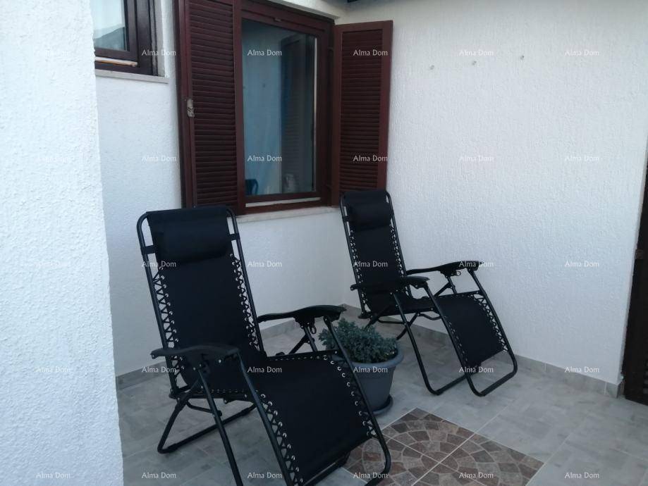 Kleine Terrasse mit zwei Liegestühlen und einem Fenster mit Fensterläden.