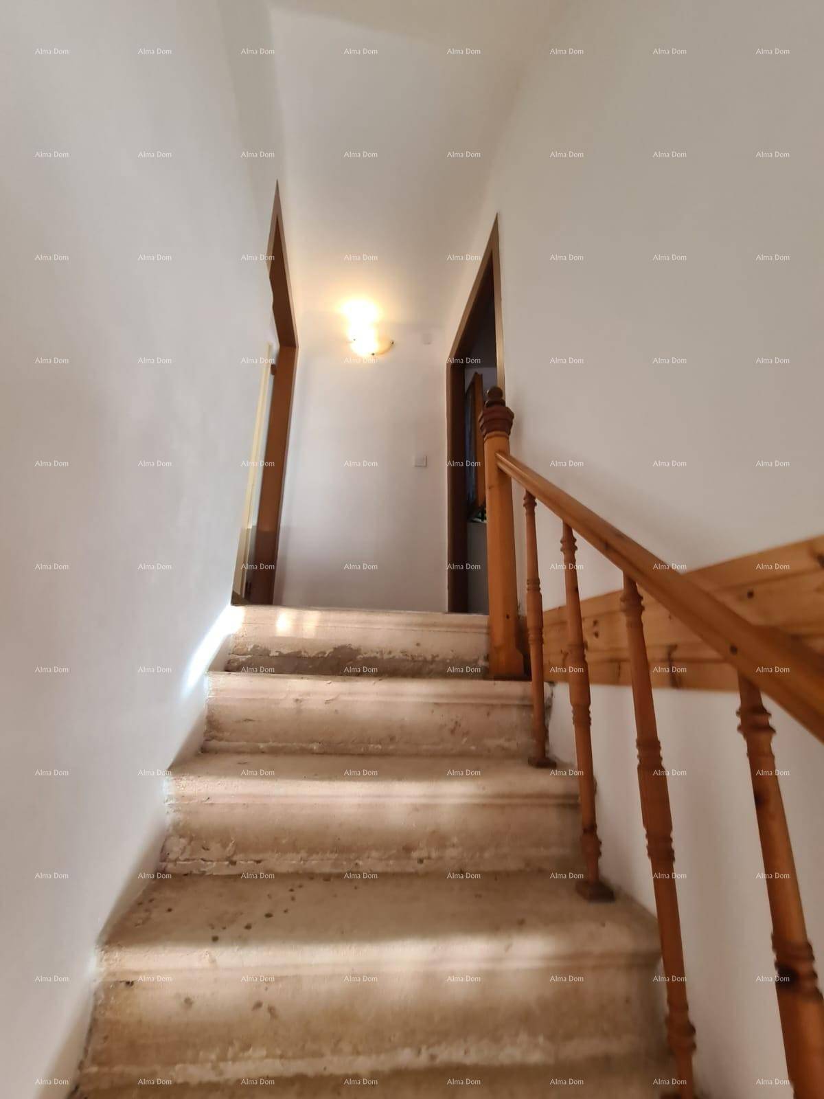 Schmale Steintreppe mit Holzgeländer führt in den oberen Bereich des Hauses, umgeben von weißen Wänden.