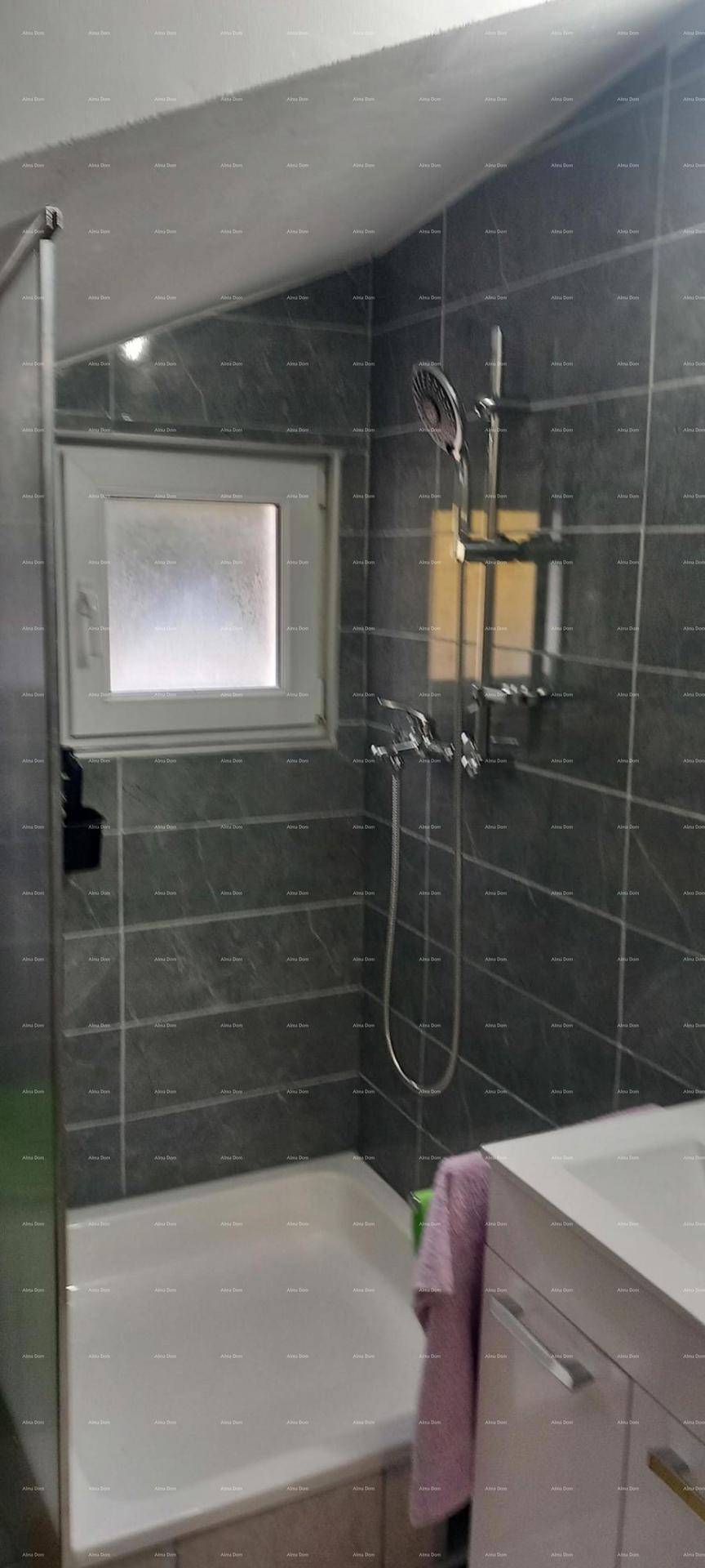 Badezimmer mit Duschkabine, grauen Wandfliesen und einem Fenster für Belüftung.