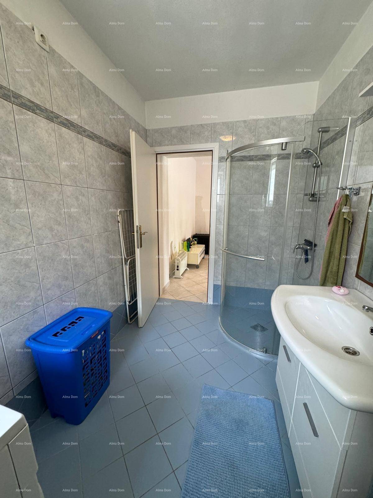 Badezimmer mit Duschkabine, Waschbecken und Zugang zu einem weiteren Raum, hell gefliest.