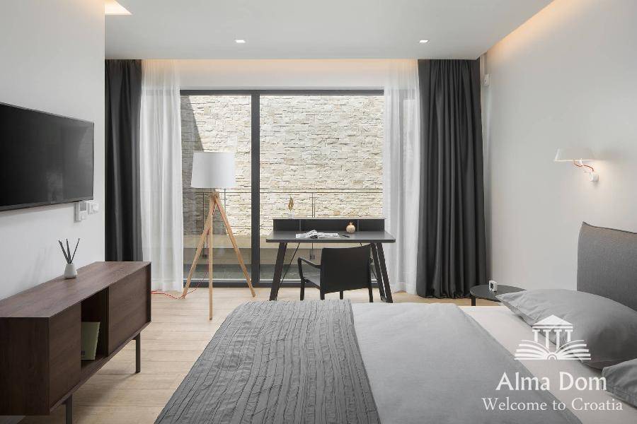 Modernes Schlafzimmer mit Arbeitsbereich, großem Fenster und Blick auf eine Steinmauer.