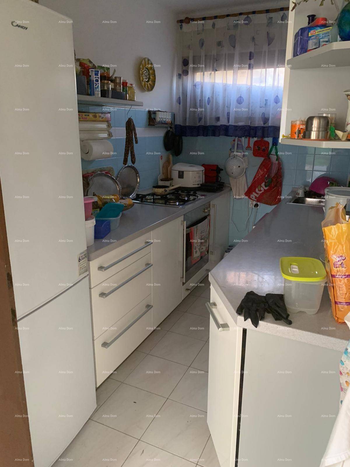 Funktionale Küche mit weißen Unterschränken, Kühlschrank, Gasherd und blauen Wandfliesen.