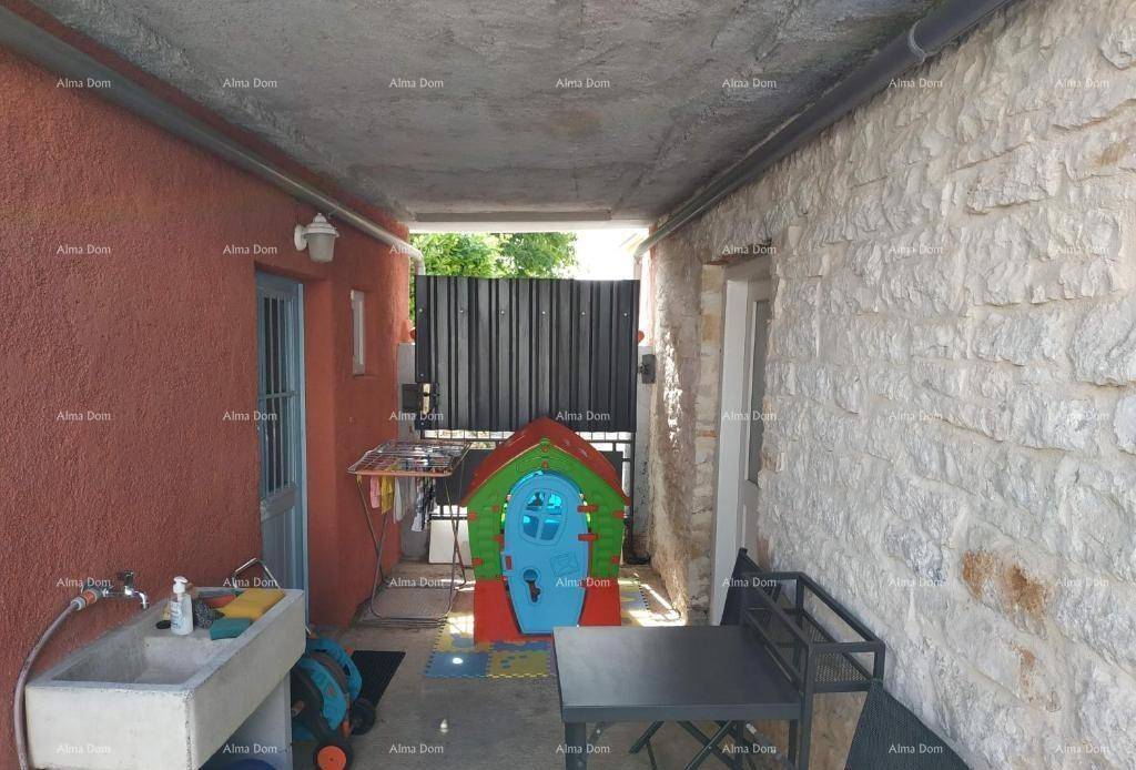 Überdachter Außenbereich mit Waschbecken, Wäscheleine und Kinderspielhaus, umgeben von Steinmauern.
