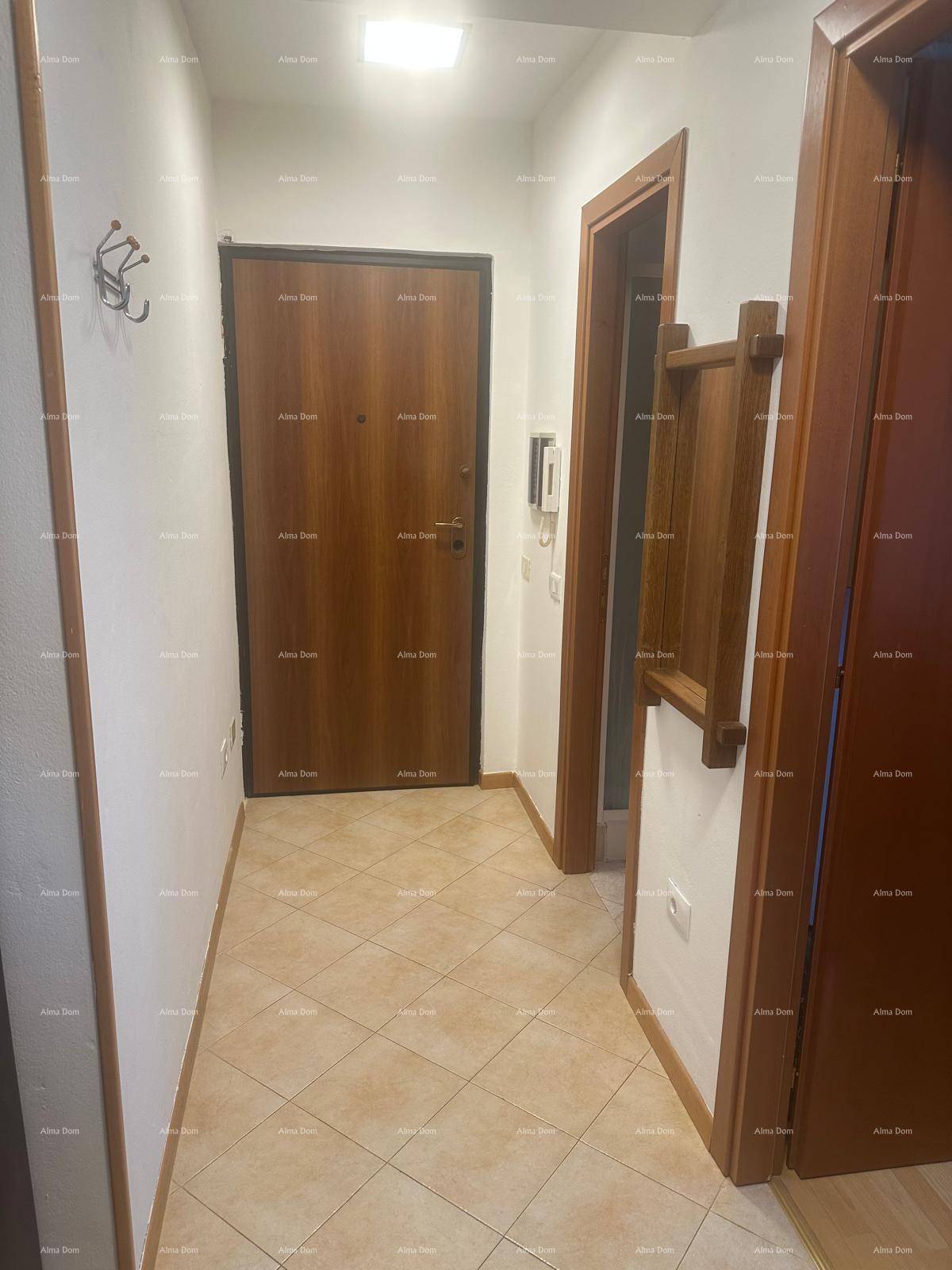 Heller Flur mit beigefarbenen Fliesen und Holztüren, ausgestattet mit Garderobe.