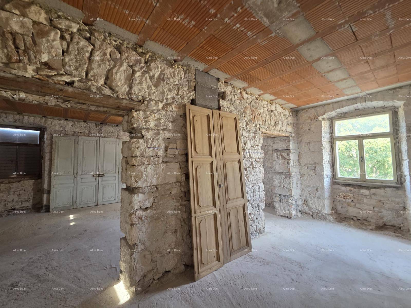 Raum im Rohbau mit freiliegenden Steinwänden, Ziegeldecke und alten Holztüren, die aufgestellt sind.