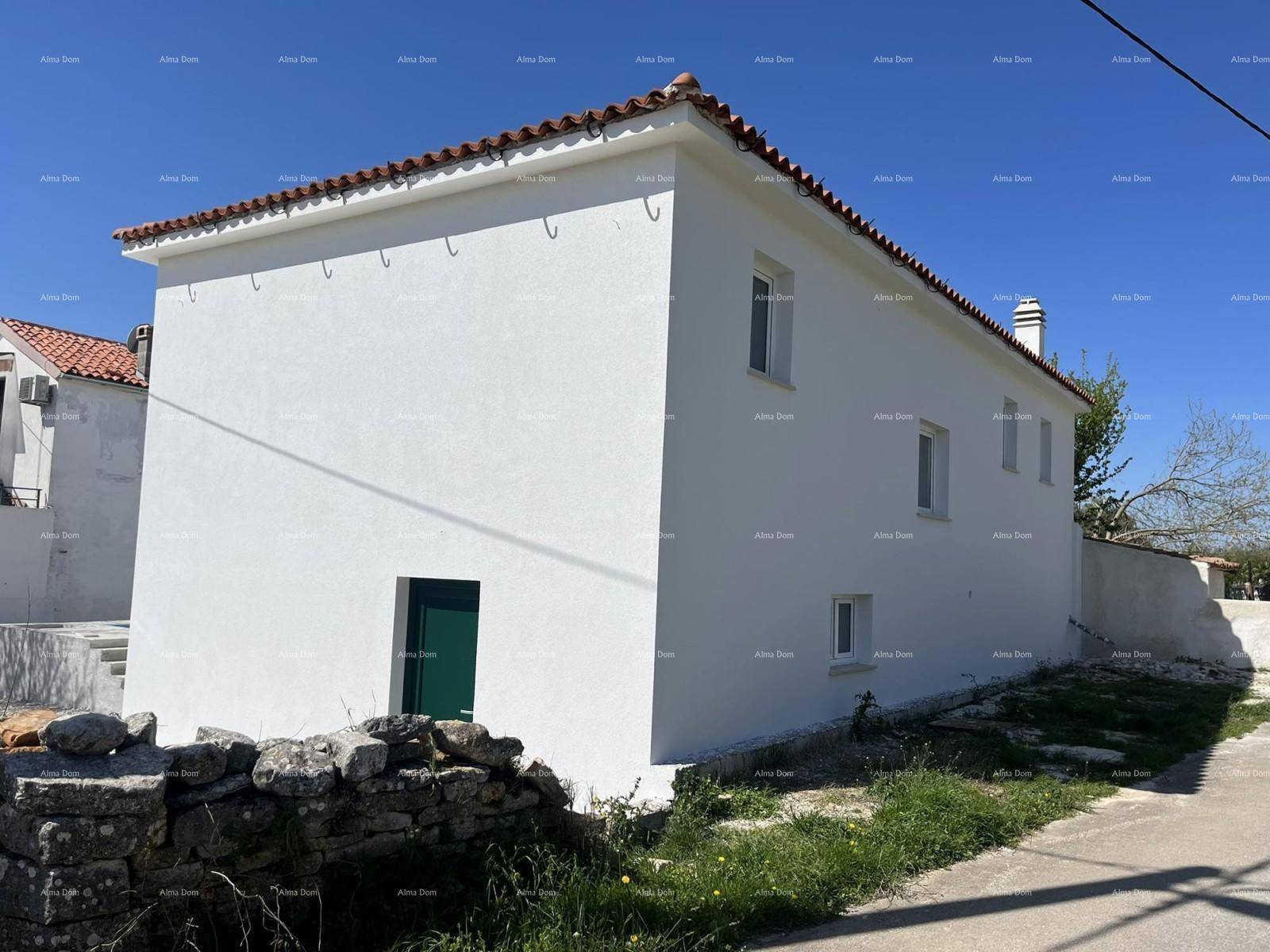 Weiß verputztes Haus im Bau mit grüner Tür und Ziegeldach unter blauem Himmel.