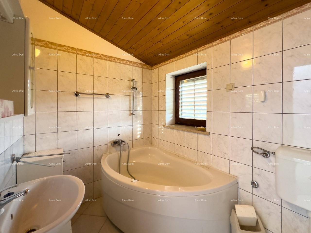 Badezimmer mit Eckbadewanne, Waschbecken, Toilette und Fenster mit Jalousien.