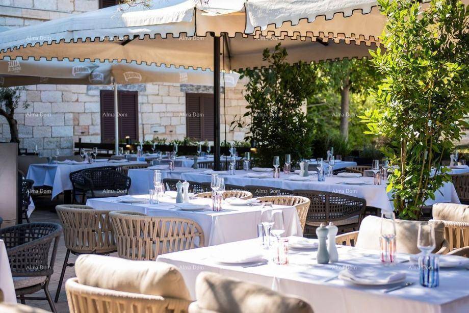Heller Restaurantbereich im Freien mit vielen Tischen, weißen Tischdecken und großen Sonnenschirmen.