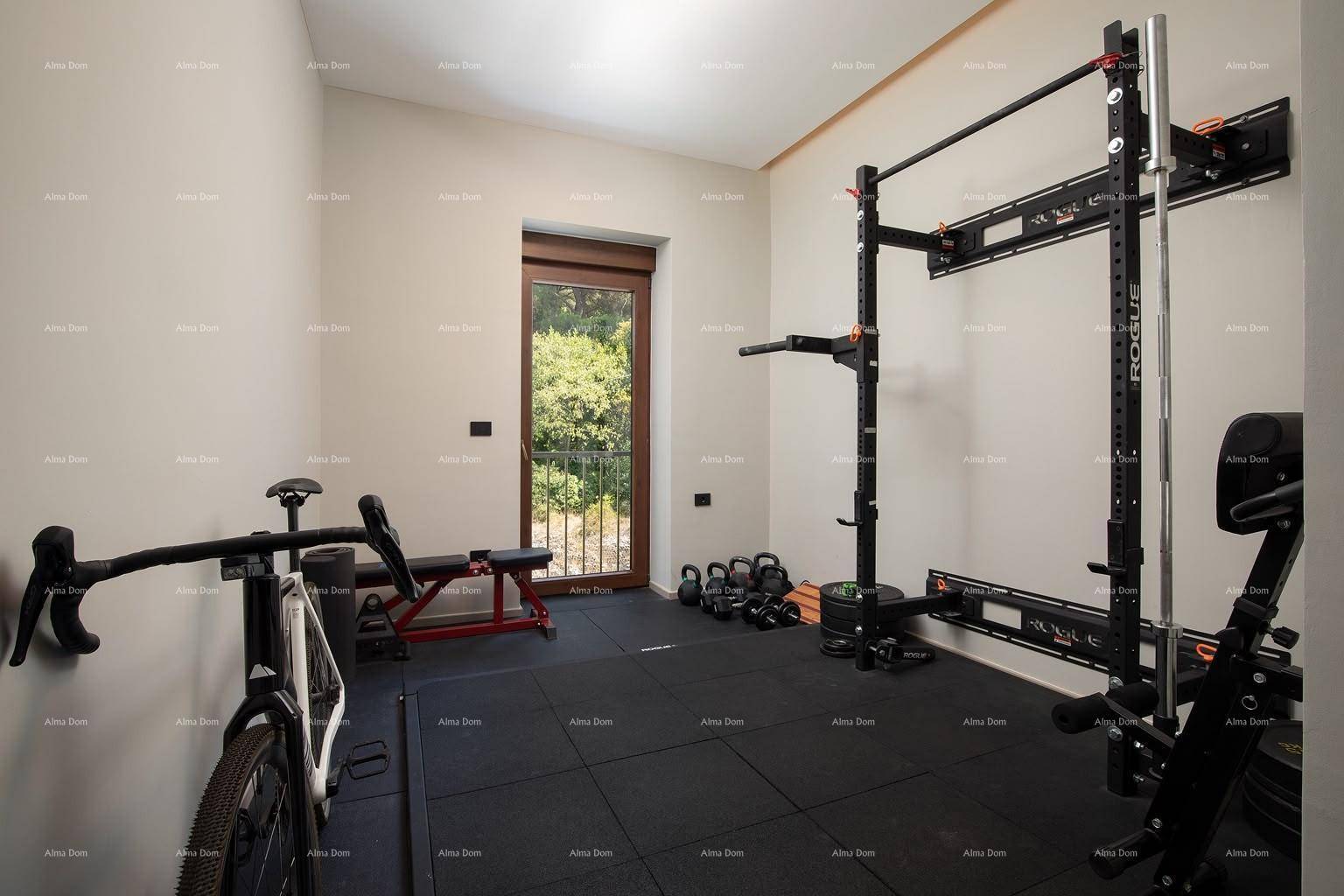 Gut ausgestatteter Fitnessraum mit Sportgeräten, Gummiboden und einem Fenster mit französischem Balkon.