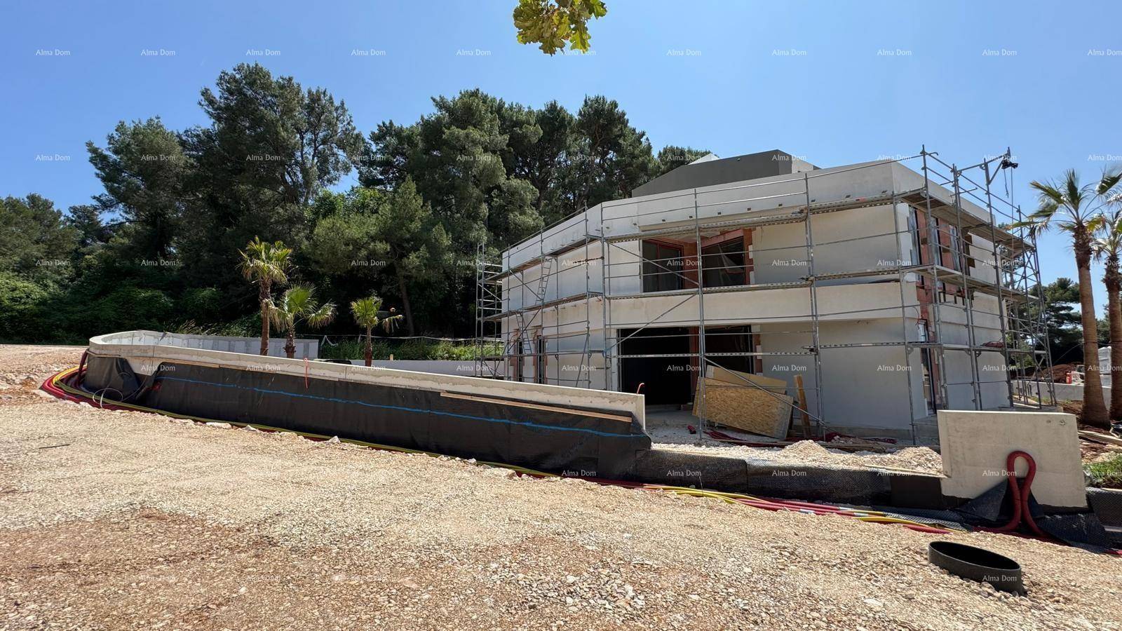 Baustelle eines modernen Hauses mit Gerüst und beginnender Fassadenverkleidung unter blauem Himmel.