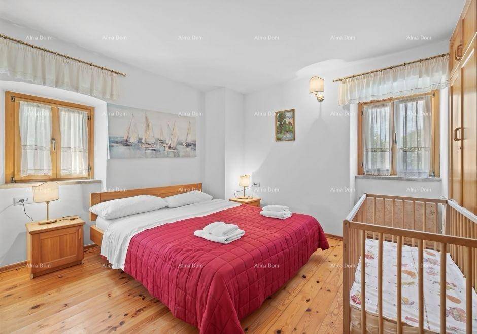 Helles Schlafzimmer mit Doppelbett, Babybett, Holzboden und zwei Fenstern.