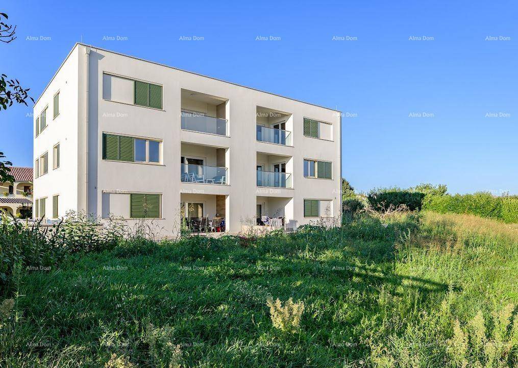 Modernes Mehrfamilienhaus mit Balkonen und umliegender Grünfläche unter blauem Himmel.