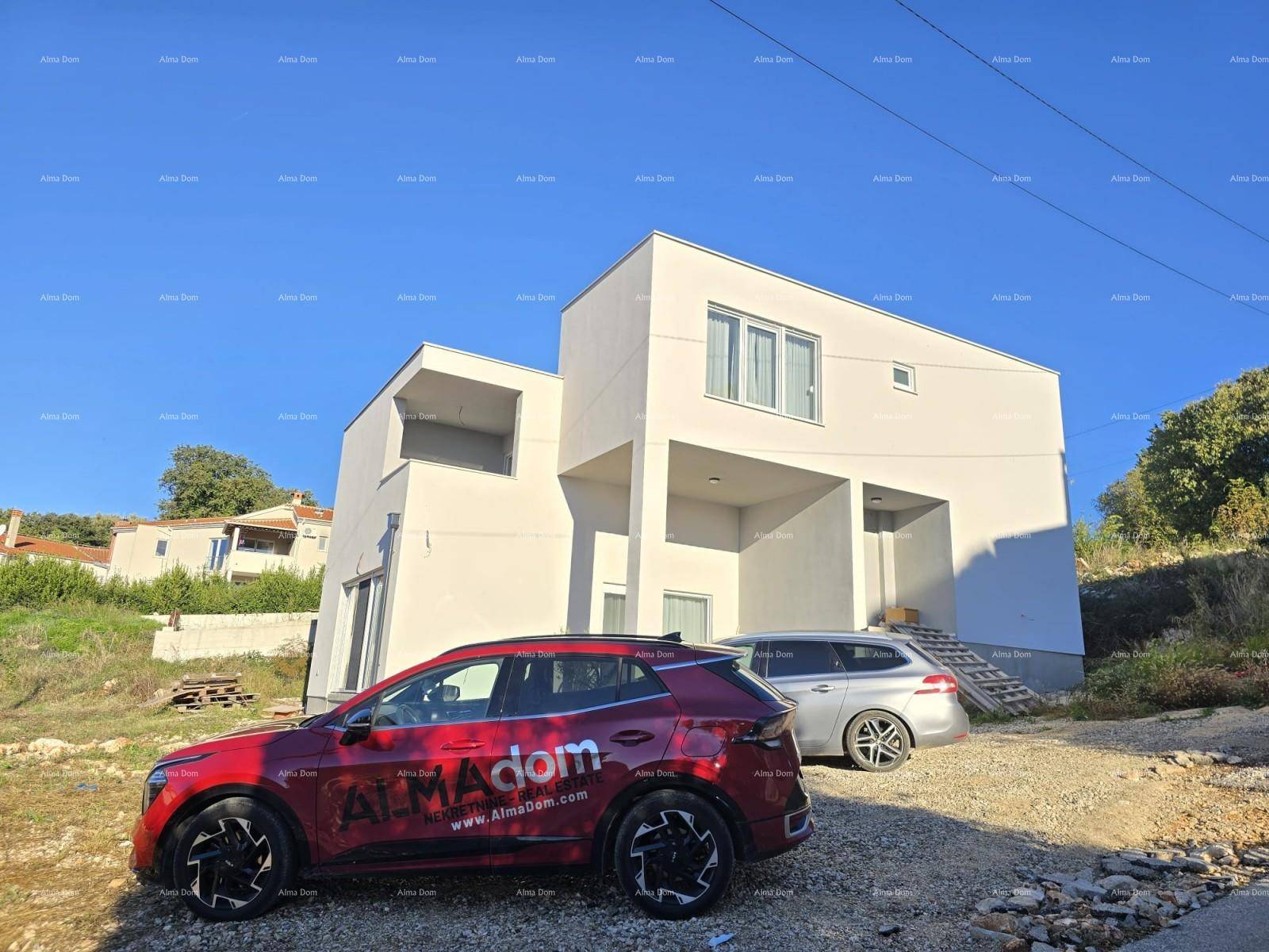 Moderne weiße Fassade des Neubaus mit klaren Linien und zwei geparkten Autos davor.