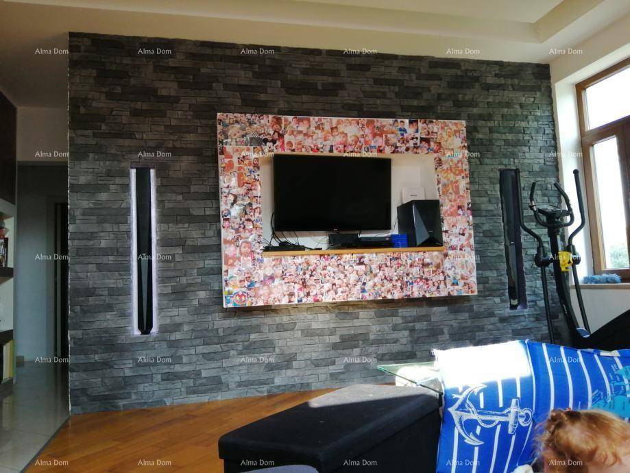 Wohnzimmer mit dekorativer Steinwand, Fernseher und Trainingsgerät am Fenster.