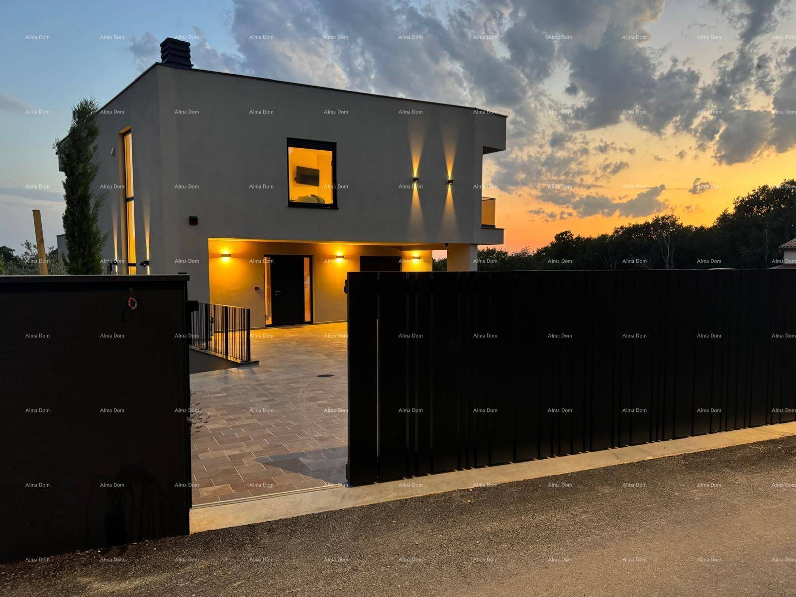 Eingangsbereich der modernen Villa mit beleuchteter Auffahrt und schwarzem Tor bei Sonnenuntergang.