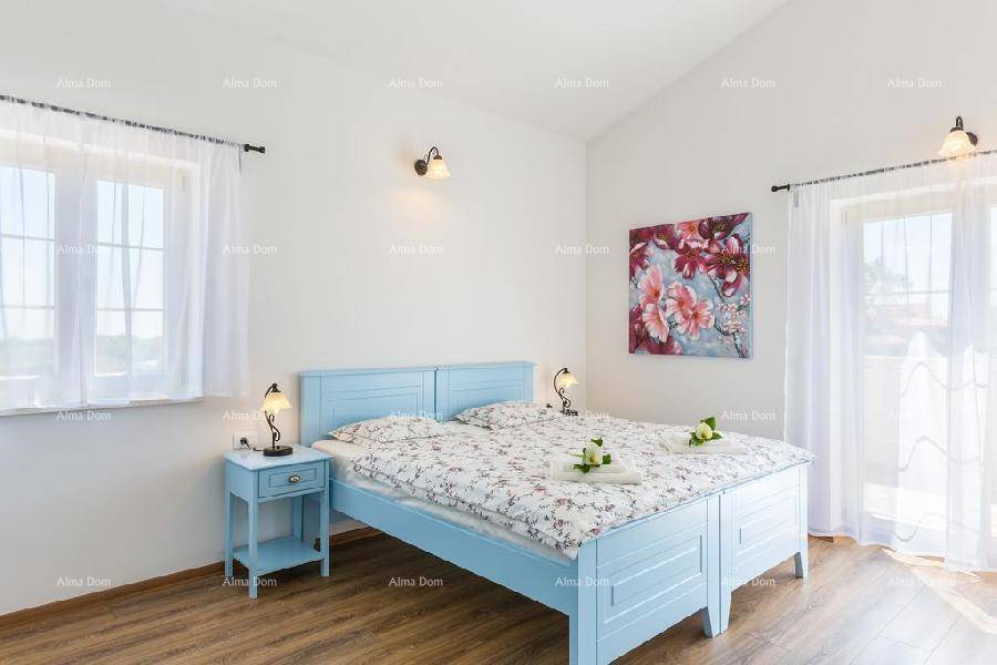 Helles Schlafzimmer mit blauem Doppelbett, Holzboden und Fenster, das viel Licht spendet.