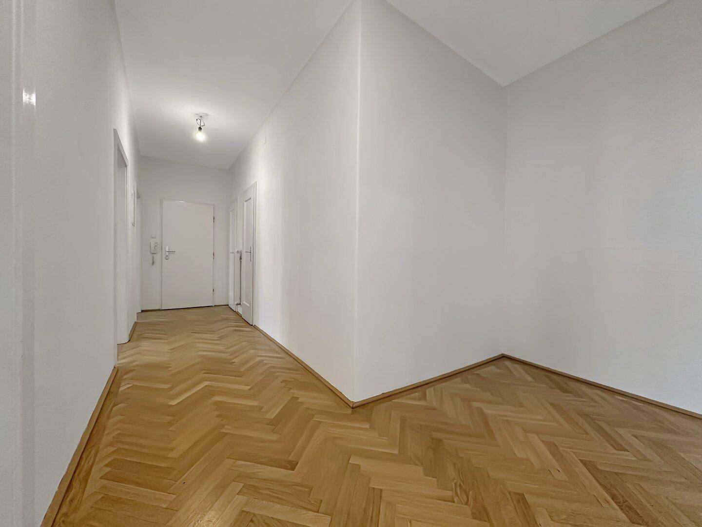 Eingangsbereich mit Fischgrätparkett und weiß gestrichenen Wänden, führt zur Wohnungstür.