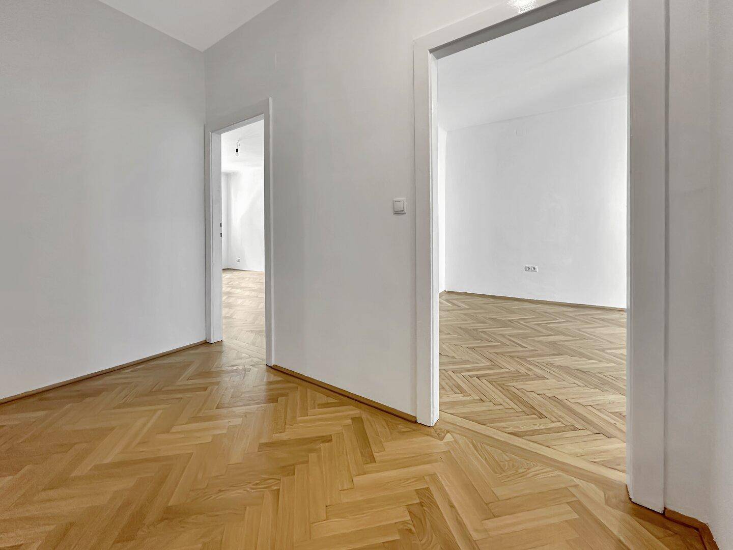 Heller Flurbereich mit Fischgrätparkett, der zu weiteren Zimmern der Wohnung führt.