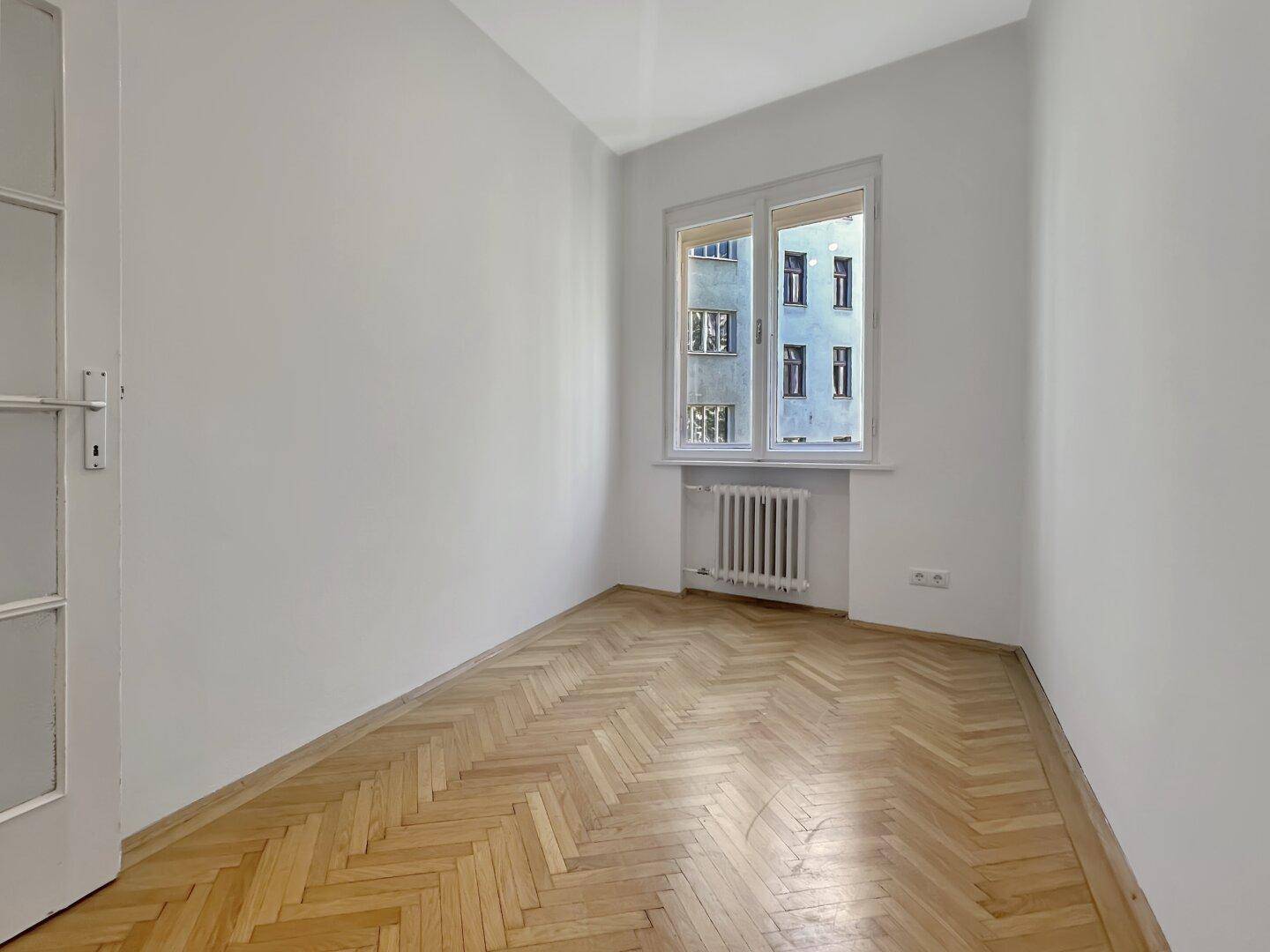 Helles Schlafzimmer mit elegantem Fischgrätparkett und einem Fenster für natürliche Belichtung.