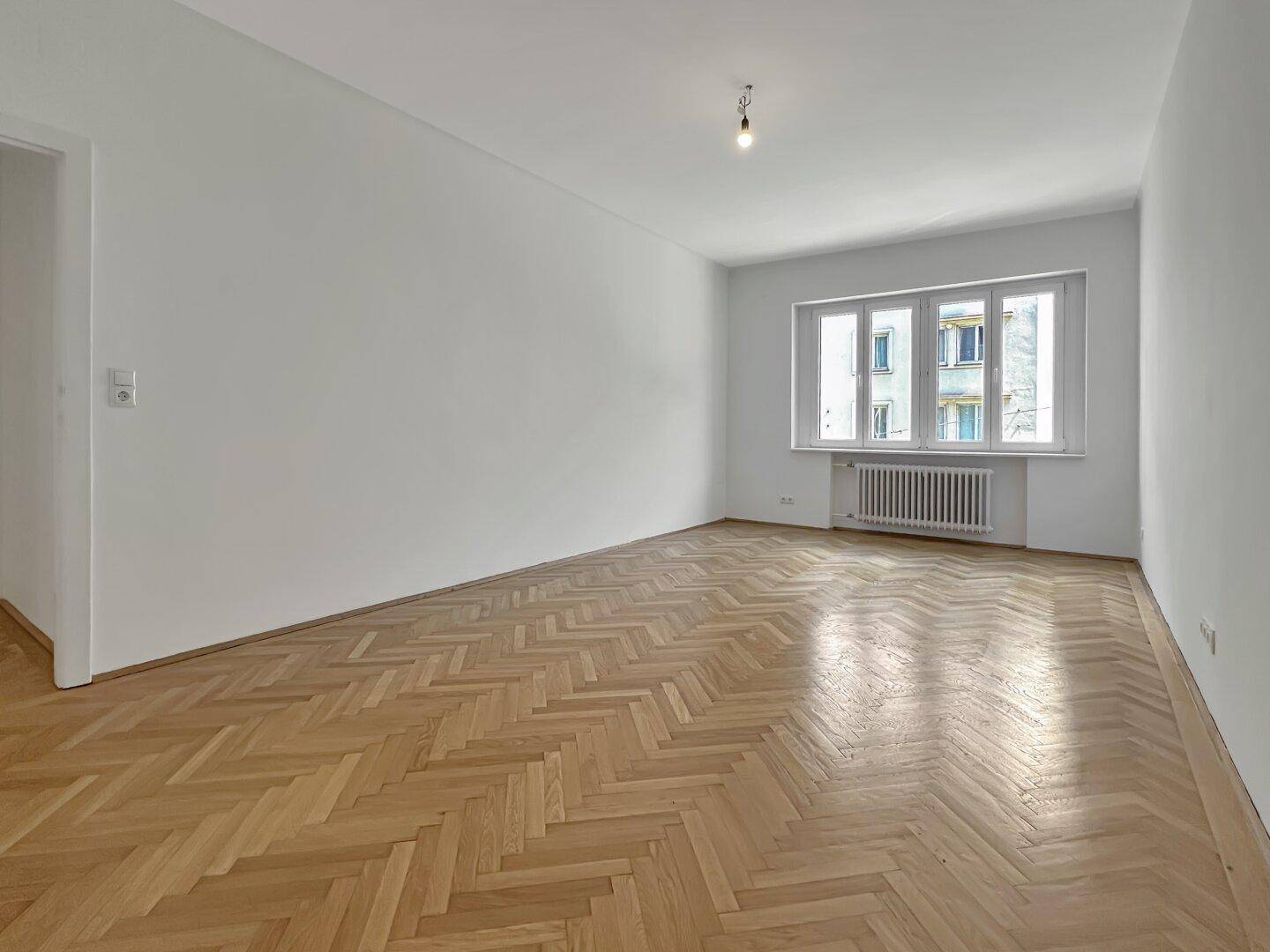 Geräumiges Zimmer mit klassischem Fischgrätparkett und viel Tageslicht durch das Fenster.