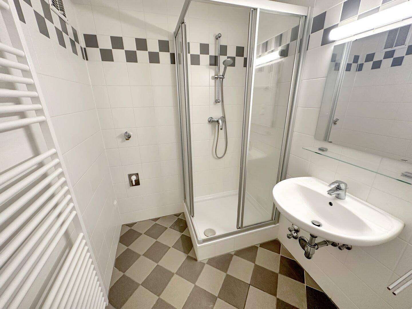 Funktionales Badezimmer mit Duschkabine, Einzelwaschbecken und beheiztem Handtuchhalter.