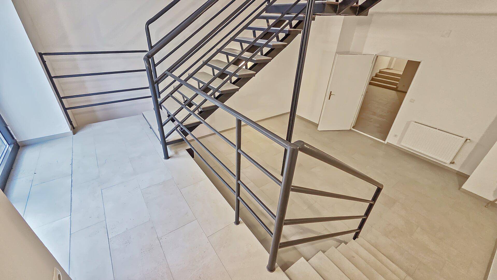 Modernes Treppenhaus im Industriestil mit offenen Metallstufen und Geländer, das zu verschiedenen Ebenen führt.