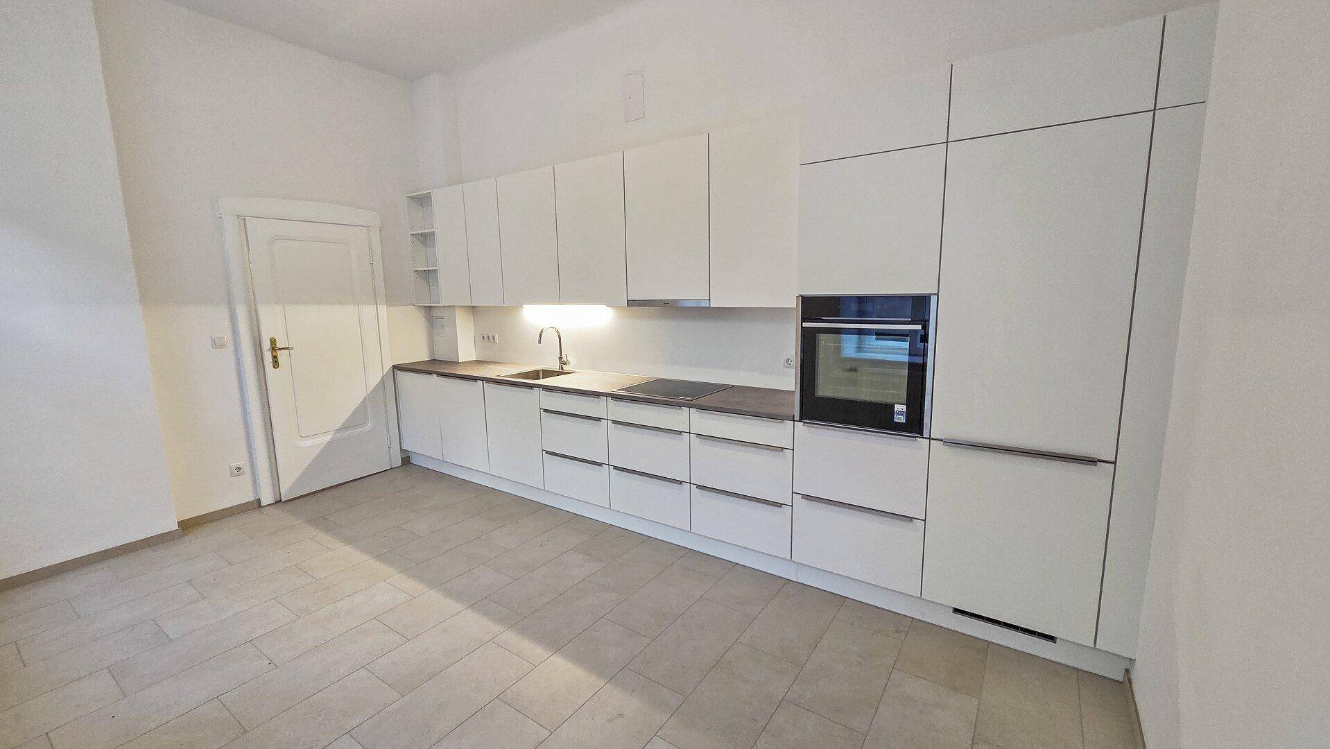 Moderne Einbauküche mit weißen, grifflosen Schränken, integriertem Backofen und heller Arbeitsplatte.