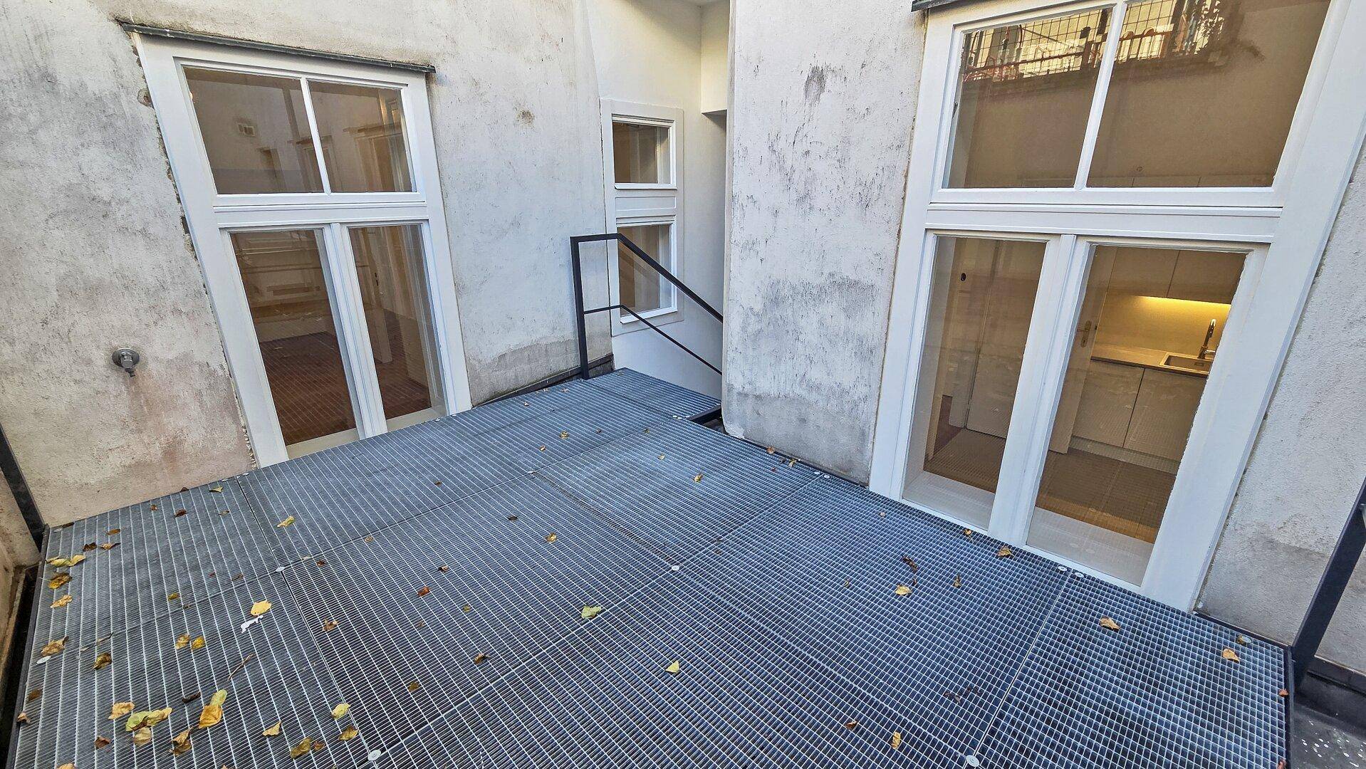 Außenbereich mit Metallgitterboden und Blick auf die umliegenden Gebäudefassaden und Fenster.