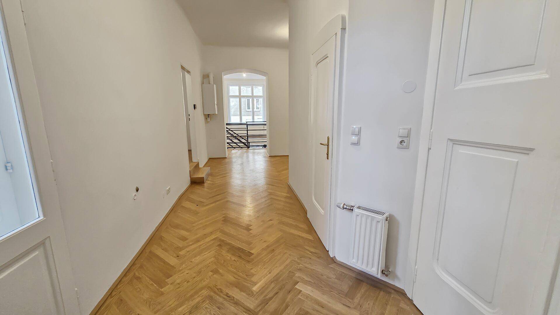 Langer, heller Flur mit Fischgrätparkett, der zu einem Treppenhaus und weiteren Räumen führt.