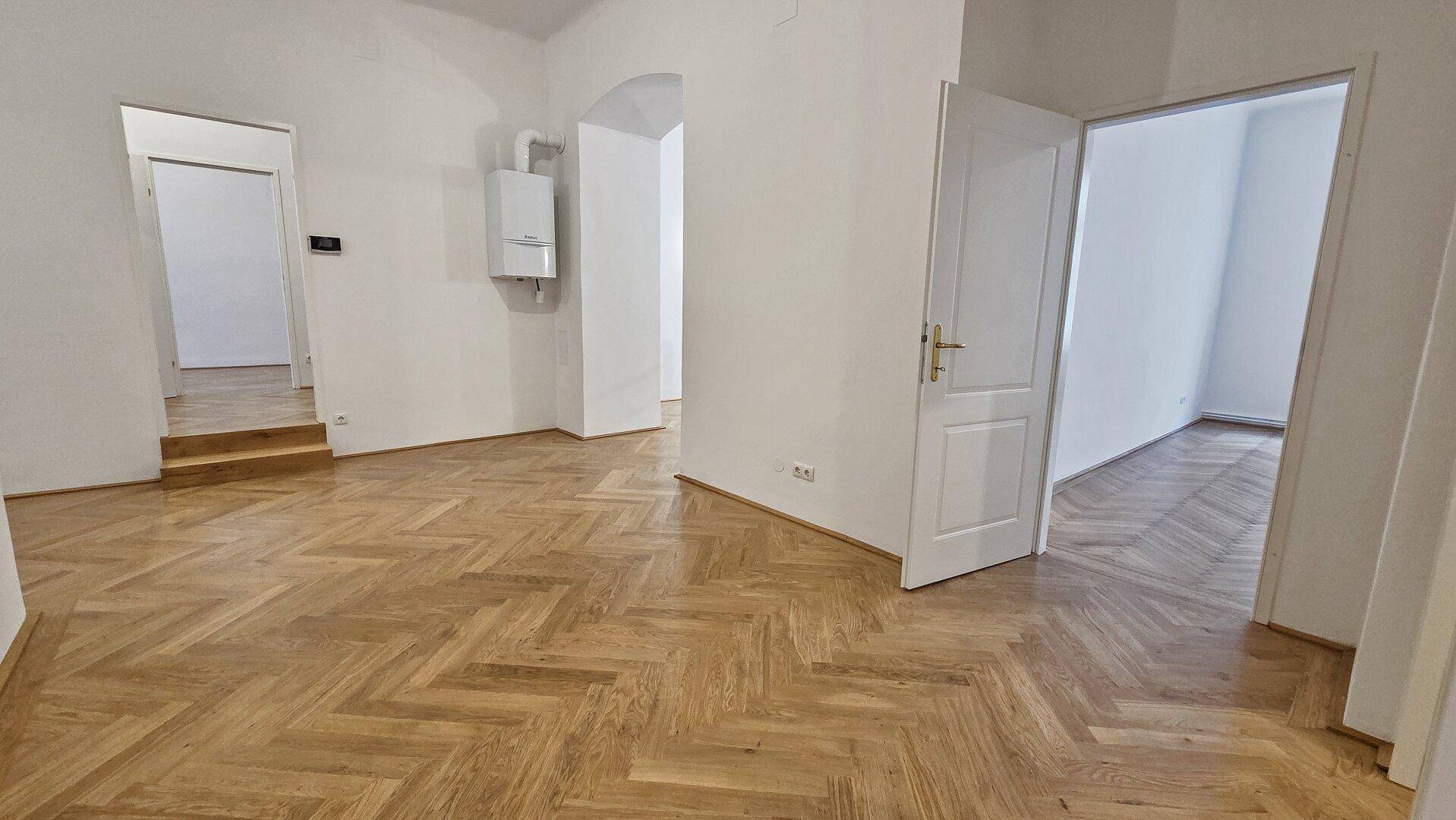 Offener Wohnbereich mit elegantem Fischgrätparkett und einem sichtbaren Heizkessel an der Wand.