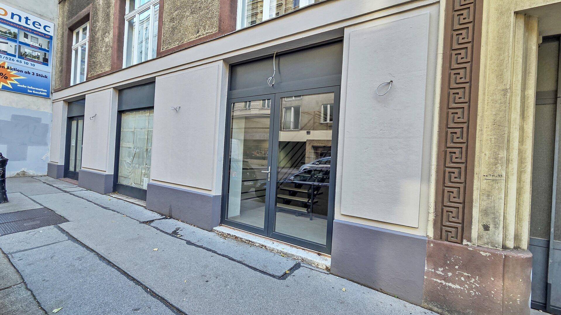 Fassade eines Geschäftsgebäudes im Erdgeschoss mit großen Schaufenstern und Eingangstüren zur Straße hin.