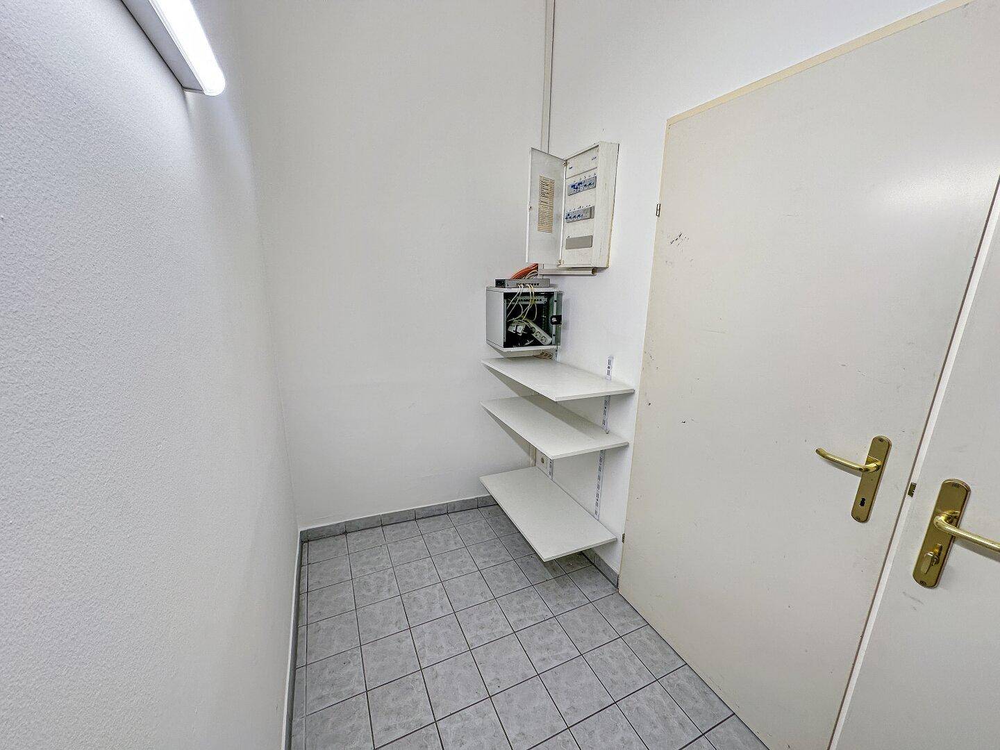 Kleiner Abstellraum mit Fliesenboden, Sicherungskasten und praktischen Wandregalen.