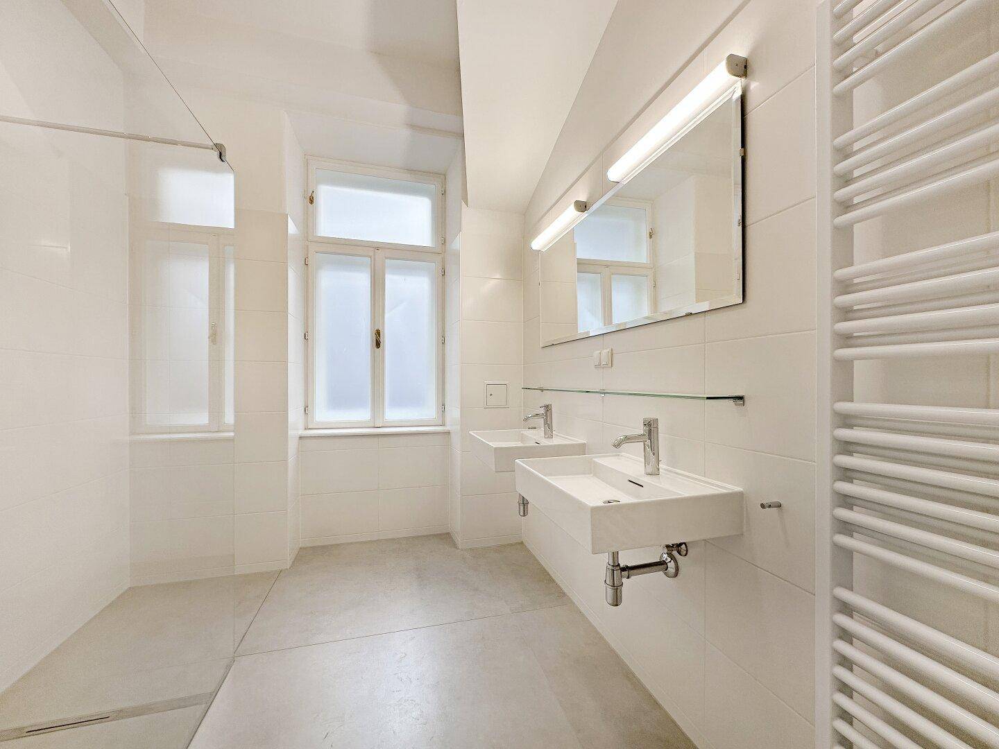 Modernes Badezimmer mit zwei Waschbecken, großer Dusche und einem Fenster für natürliches Licht.