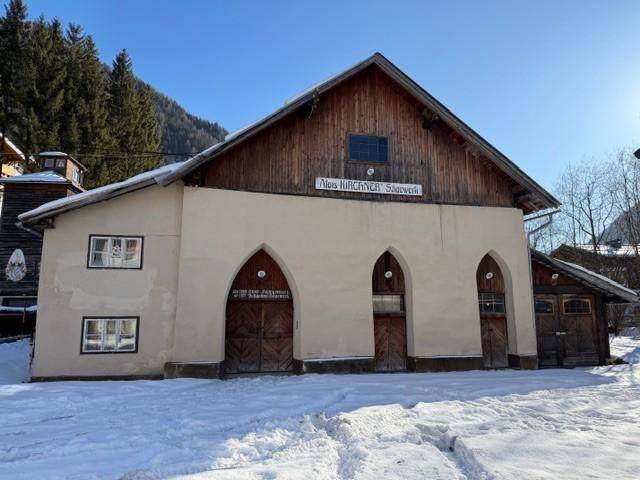 Traditionelles Gebäude mit heller Fassade, Holzdach und drei großen Rundbogeneingängen im Schnee.