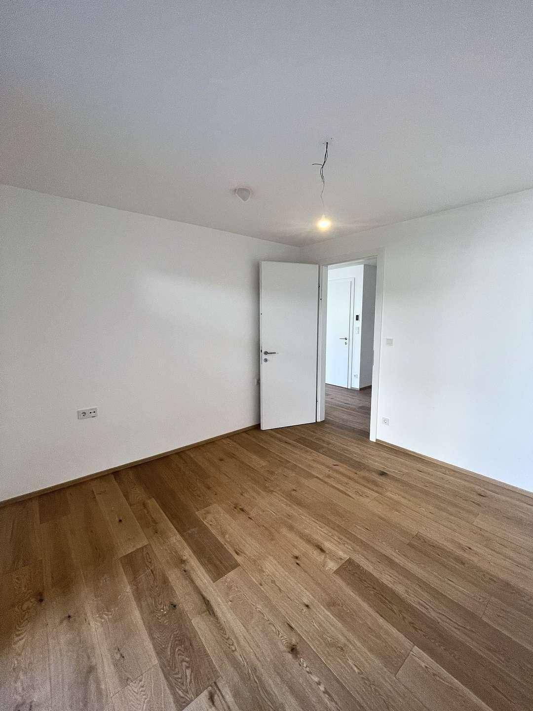 Schlafzimmer mit Holzboden und weiß gestrichenen Wänden, bereit zur individuellen Gestaltung.