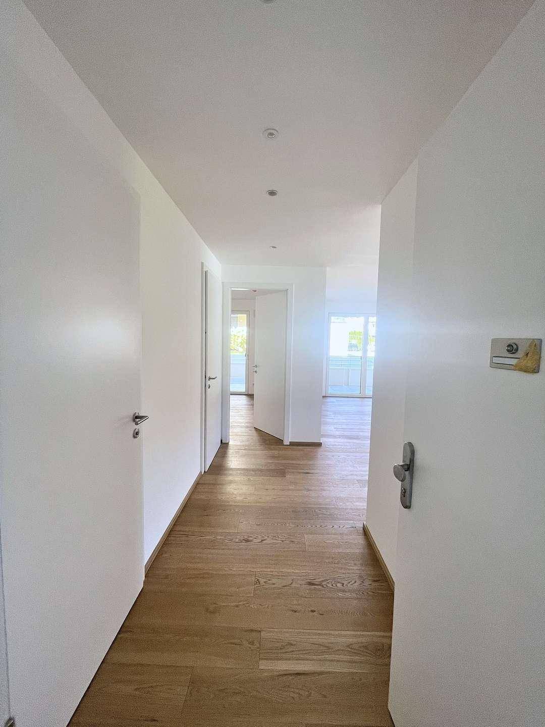Heller Flur mit Holzboden und weißen Wänden, der zu den verschiedenen Räumen führt.