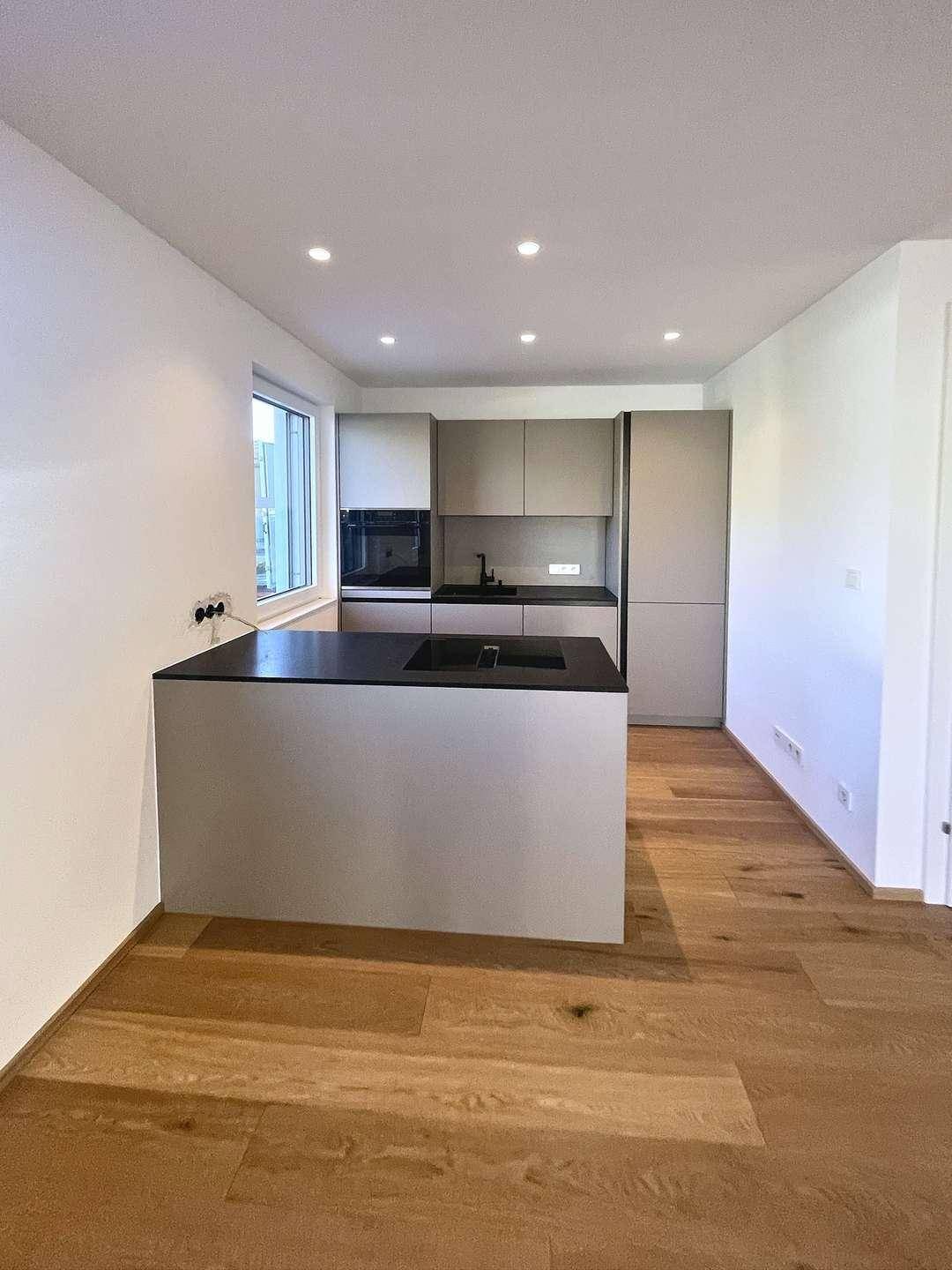 Moderne Einbauküche mit Kücheninsel, dunkler Arbeitsplatte und integrierten Geräten.
