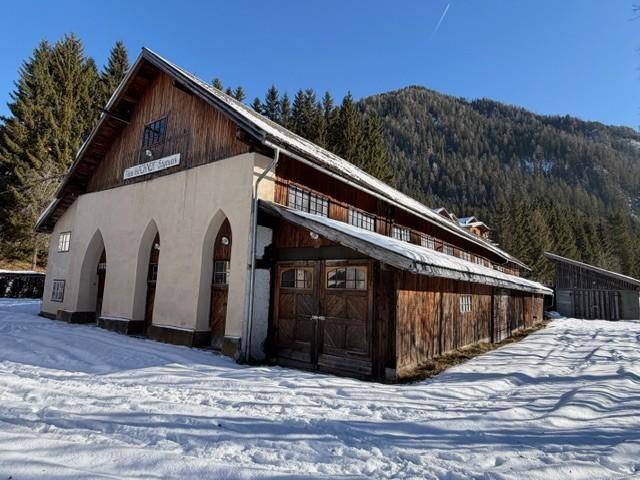 Großes, historisches Gebäude mit Holzdach und Rundbögen, umgeben von Schnee und Wald.