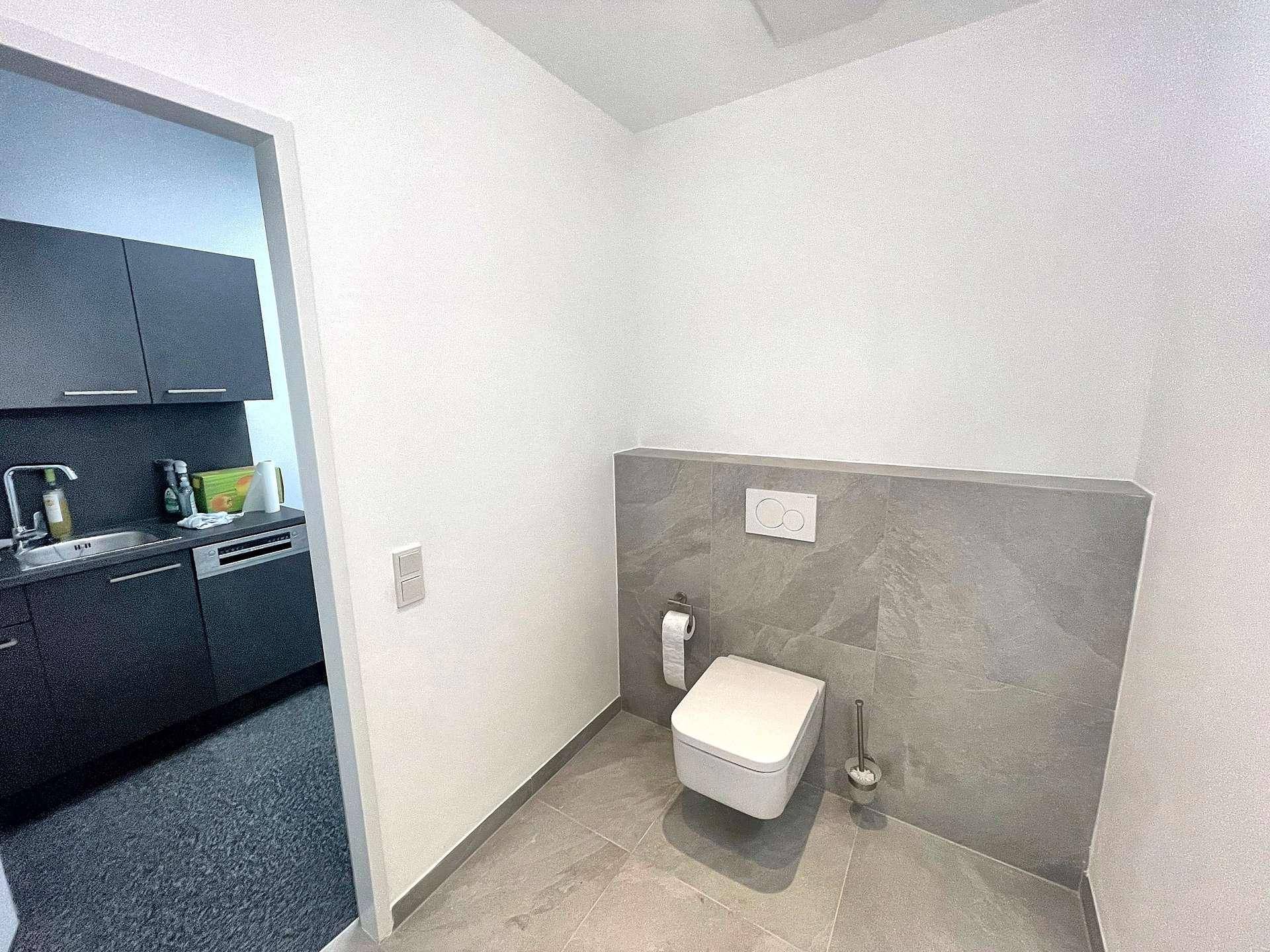 Modernes Gäste-WC mit wandhängender Toilette und grauen Fliesen an Wand und Boden.