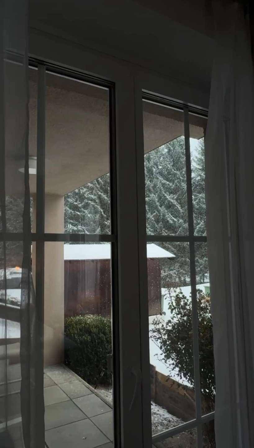 Blick aus dem Fenster auf eine verschneite Landschaft mit Bäumen und einem Gebäude.