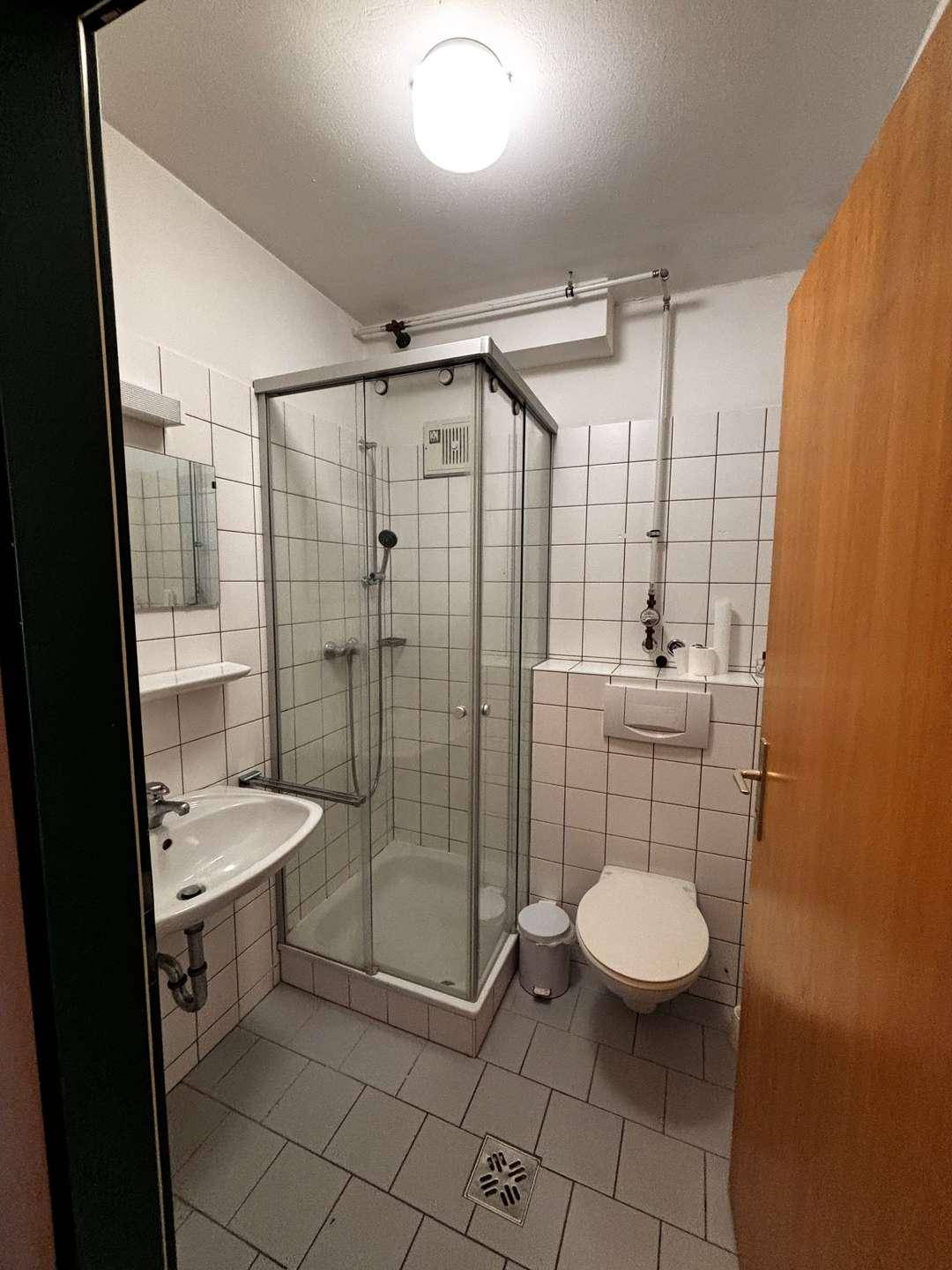 Funktionales Badezimmer mit Duschkabine, WC, Waschbecken und weißen Fliesen an Wänden und Boden.