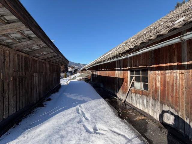 Schmaler, verschneiter Weg zwischen zwei rustikalen Holzgebäuden unter klarem Himmel.