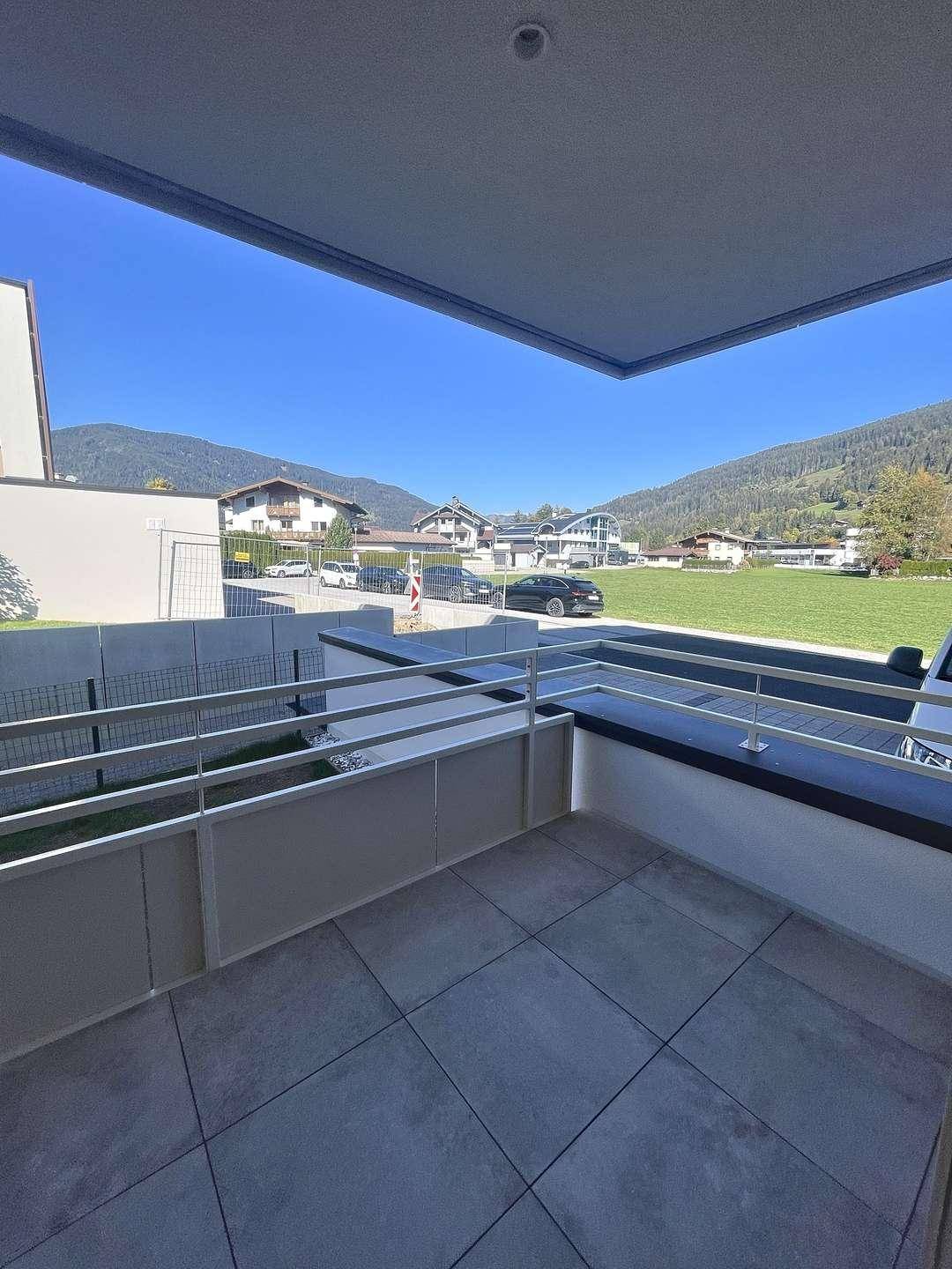 Balkon mit Fliesenboden und Blick auf die umliegende Berglandschaft und grüne Wiesen.