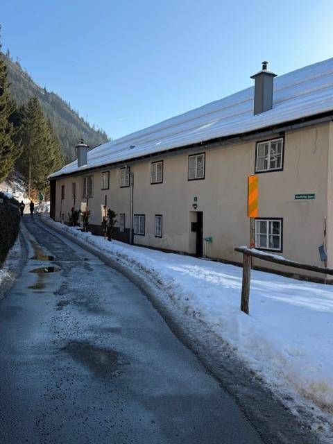 Langes, traditionelles Gebäude entlang einer verschneiten Straße mit Blick auf bewaldete Berge.