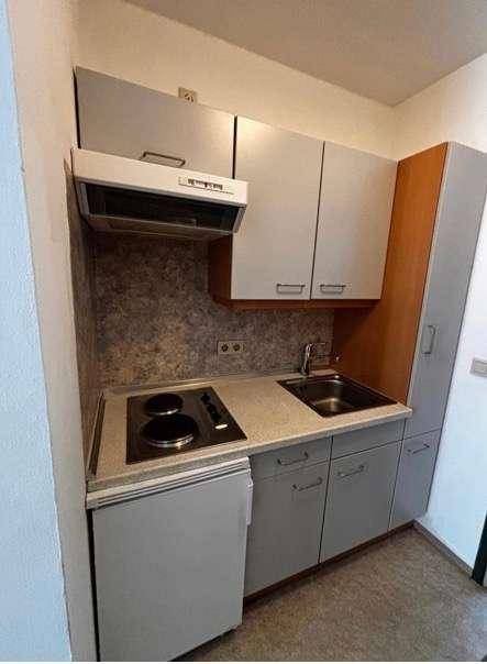 Kleine Küchenzeile mit Spüle, Kochfeld und Kühlschrank in kompakter Anordnung.