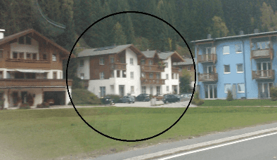 Mehrere Gebäude in alpiner Umgebung mit bewaldeten Bergen im Hintergrund und einer Straße im Vordergrund.