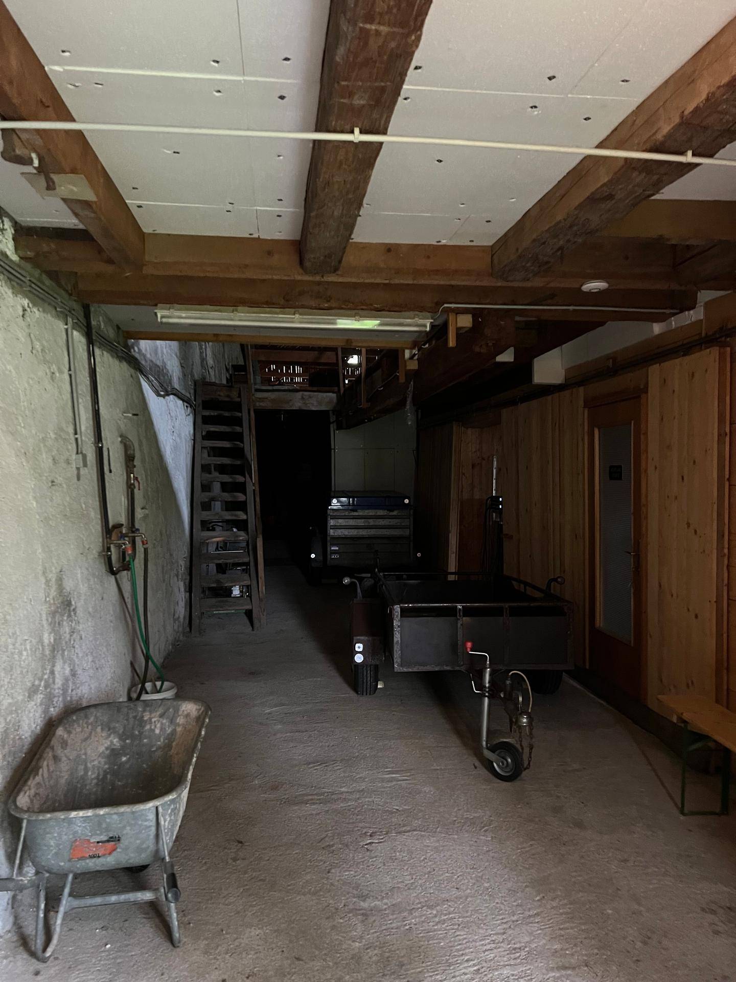 Geräumiger Lagerraum oder Werkstatt mit Holzbalkendecke, Betonboden und verschiedenen Geräten.
